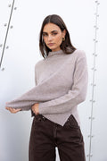 Woman wearing a gray sweater and dark jeans against a white background
