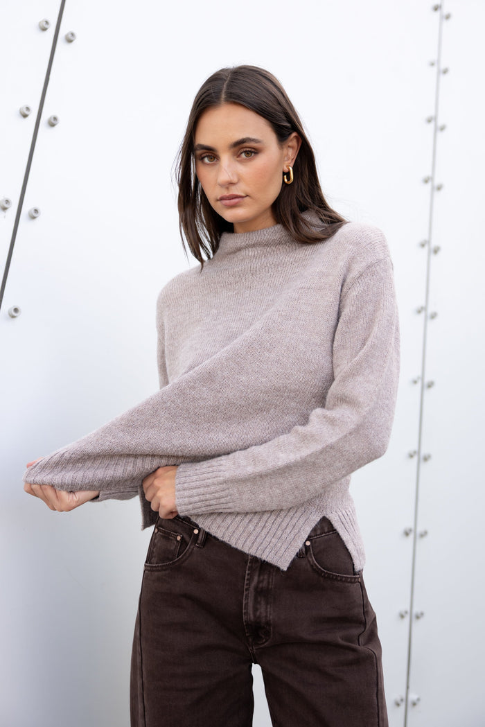 Woman wearing a gray sweater and dark jeans against a white background