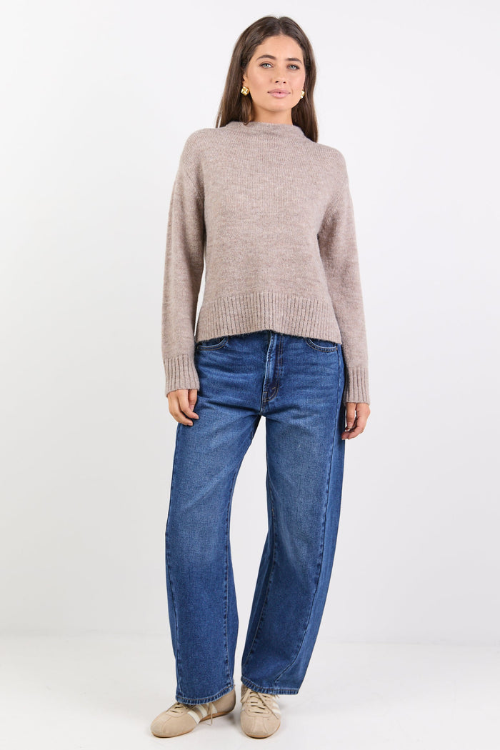 Woman wearing a beige sweater and blue jeans on a white background