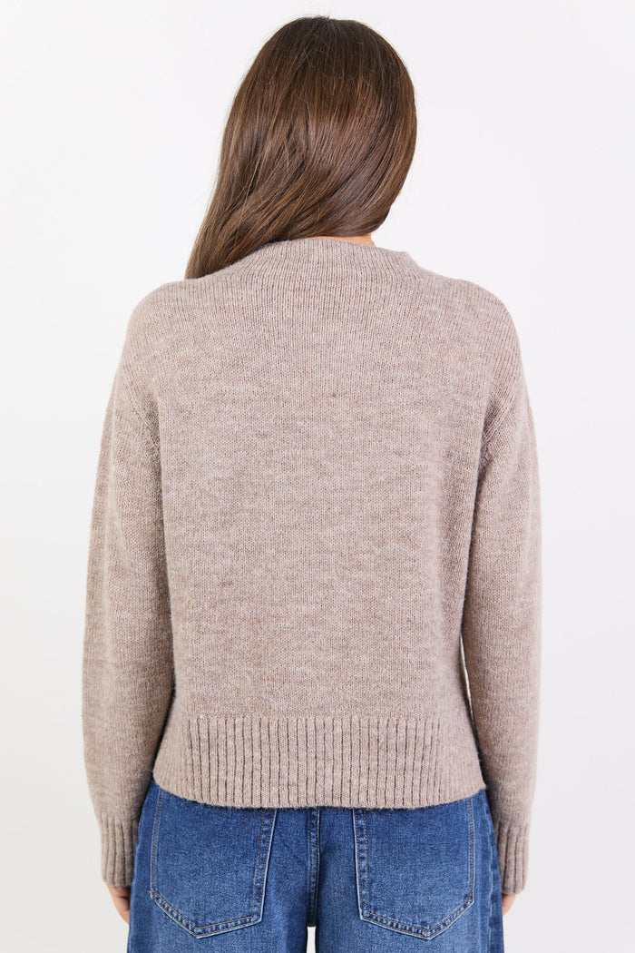 Person wearing a beige sweater and blue jeans on a white background