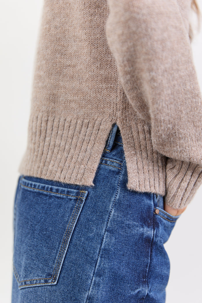 Close-up of a person wearing a beige sweater and blue jeans on a light background