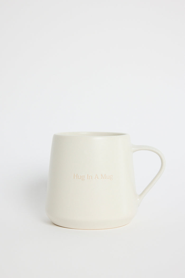 Cream-coloured ceramic mug with the words ‘Hug In A Mug’ embossed on the front, photographed on a white background