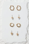 Set of gold earrings on a white stone display block against a beige background