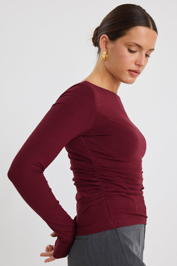 Model wears a burgundy stretch long sleeve top with grey pants.