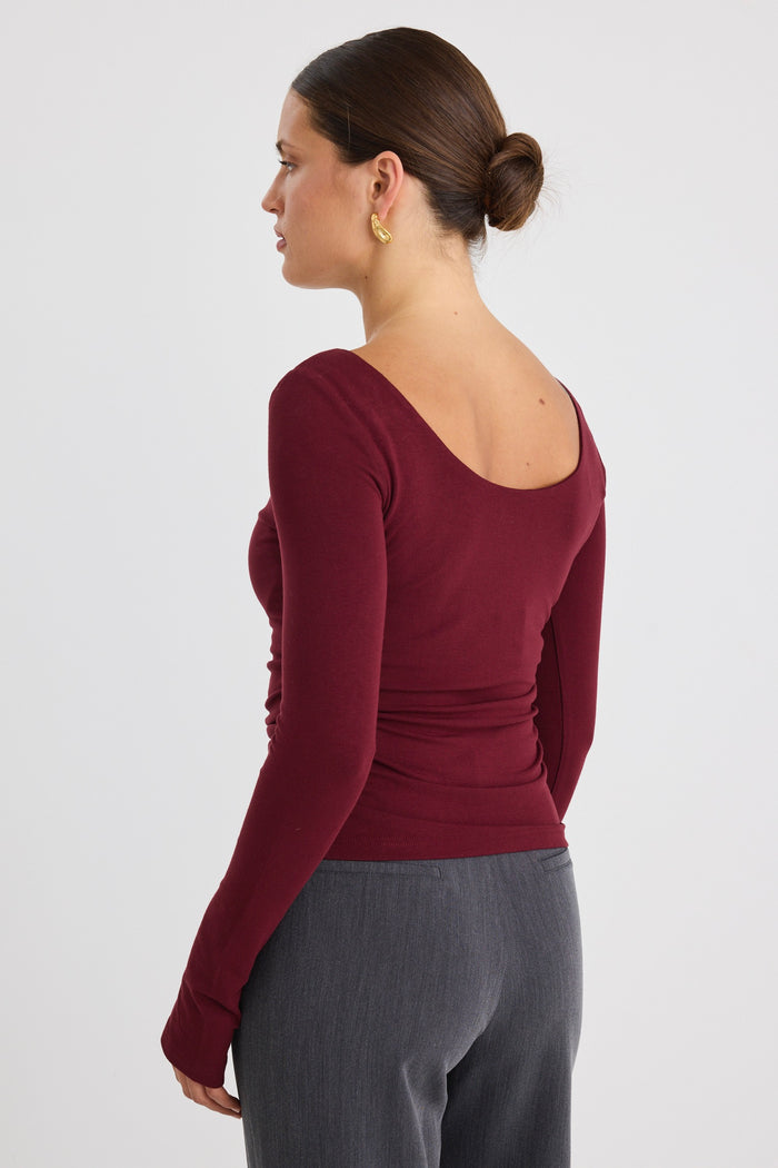 Model wears a burgundy stretch long sleeve top with grey pants.