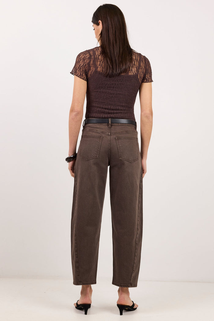 A woman is shown from the back wearing a dark brown lace short-sleeve top, brown wide-leg cropped pants, a black belt, and black heels, set against a plain white studio background.