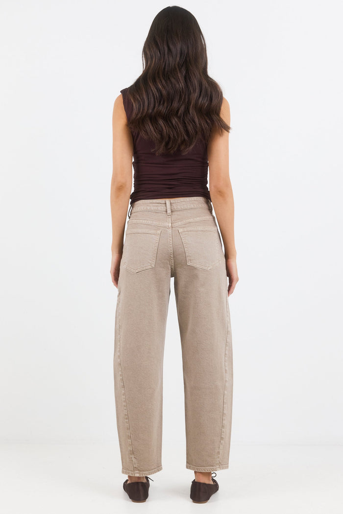 Woman wearing beige pants and a brown top on a white background