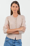 Woman wearing a beige cardigan and blue jeans with a white background