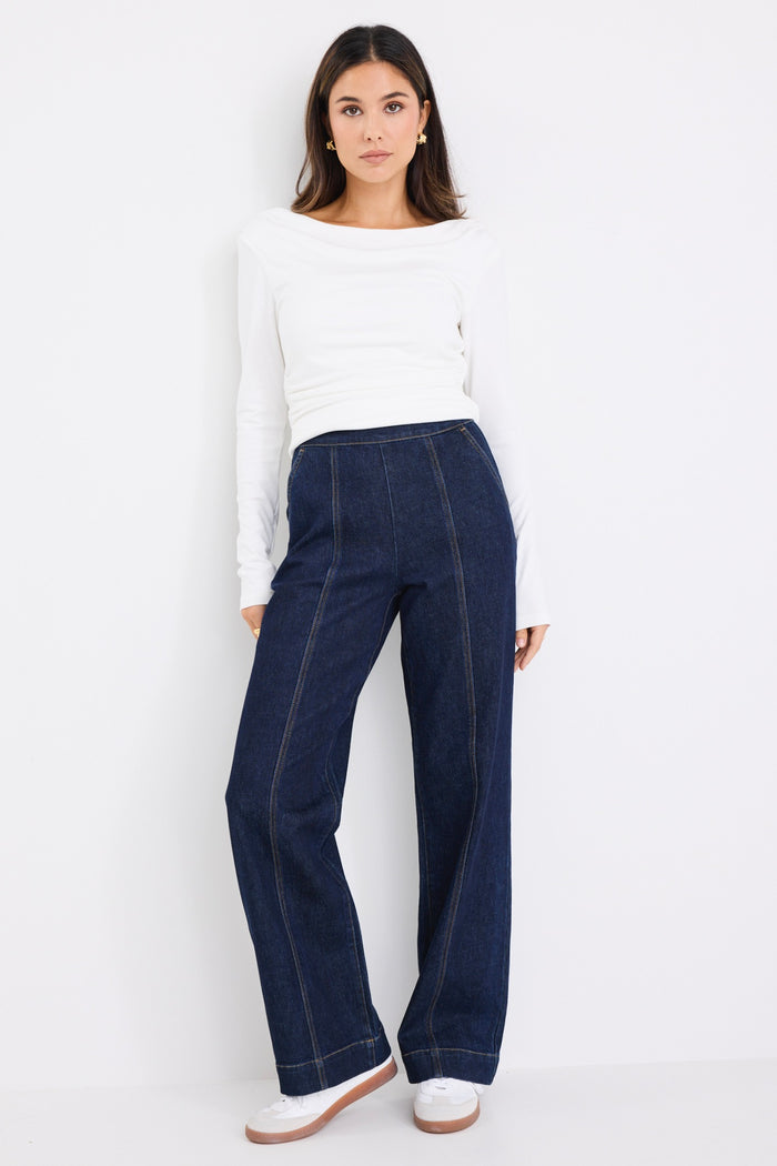 model wears dark blue jeans with a white long sleeve top