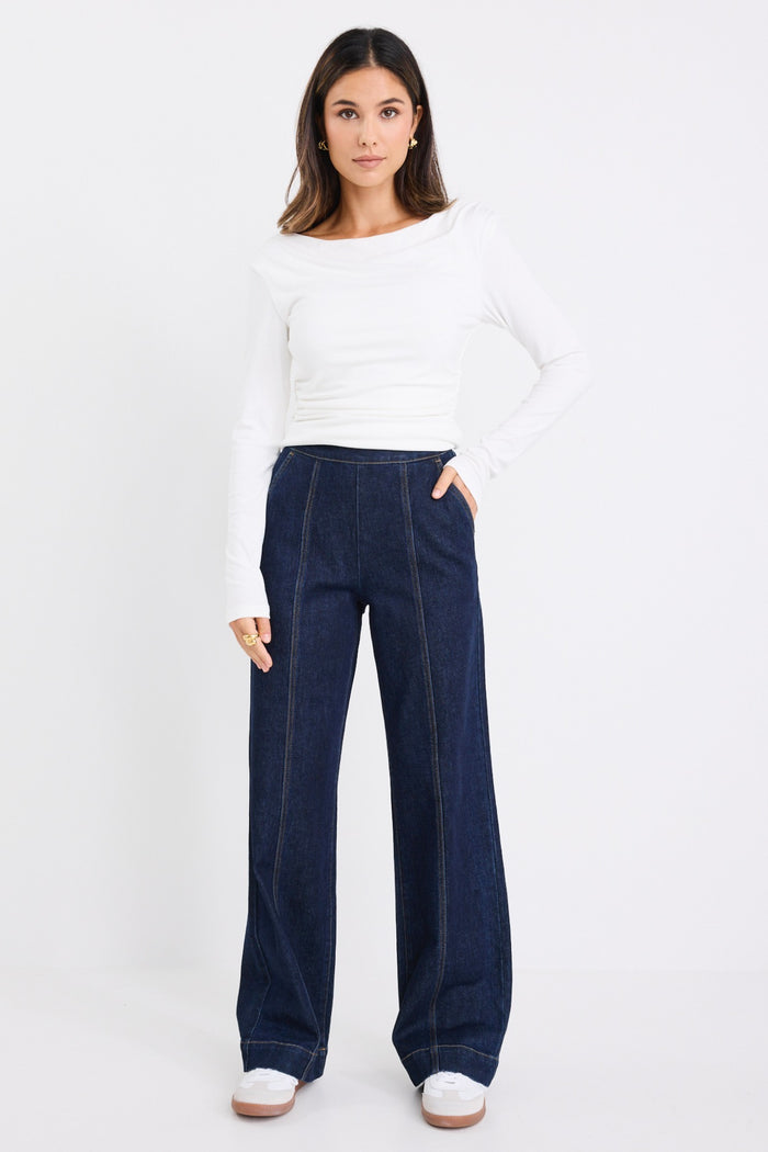 model wears dark blue jeans with a white long sleeve top