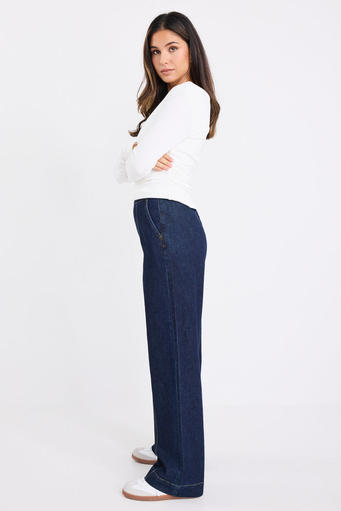 model wears dark blue jeans with a white long sleeve top