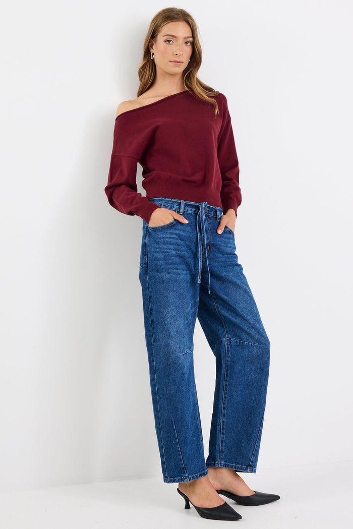 Woman wearing a burgundy off-shoulder top and blue jeans on a white background