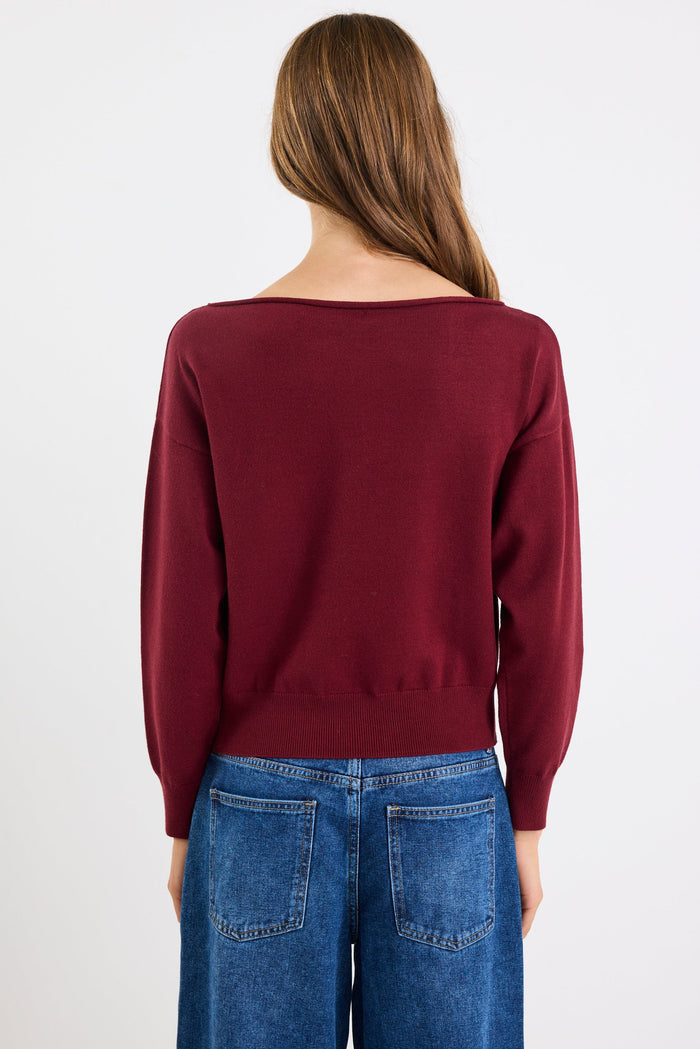 Person wearing a burgundy sweater and blue jeans on a white background