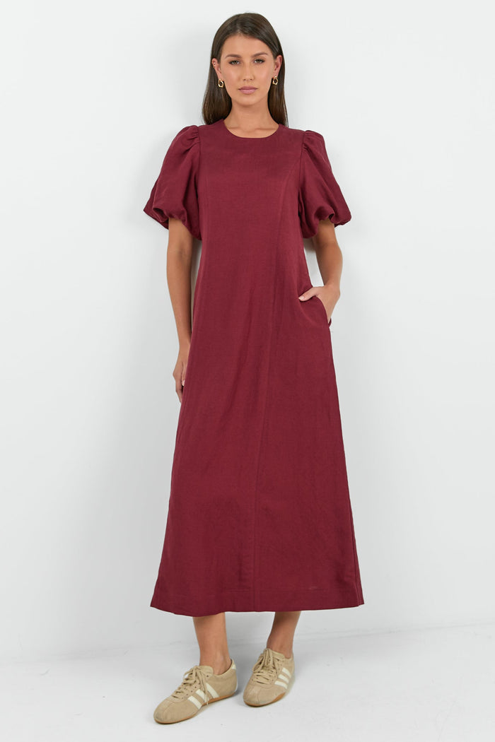 Woman wearing a burgundy dress with ruffled sleeves on a white background