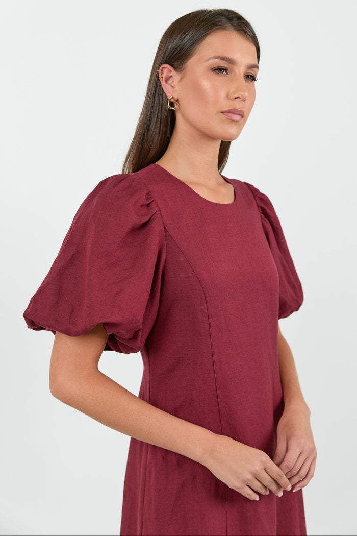 Woman wearing a burgundy dress with puffed sleeves against a white background