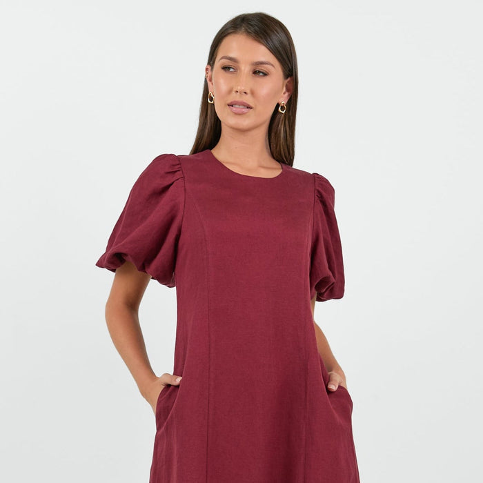 Woman wearing a burgundy dress with puff sleeves on a white background