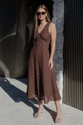 Woman in a brown polka dot dress standing against a textured wall.
