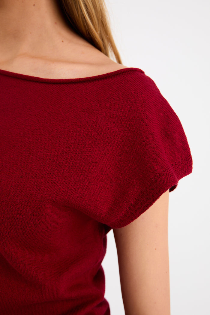 Model wearing a cherry red sleeveless knit top with a boatneck neckline