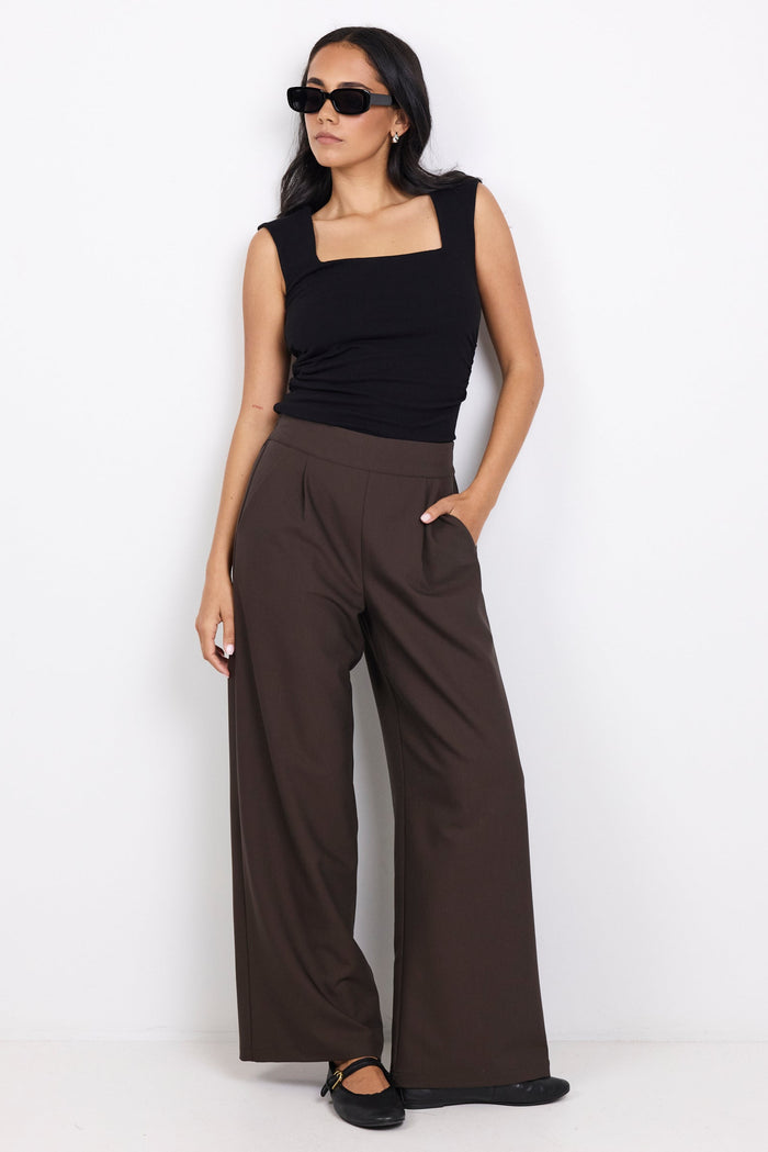 Woman wearing a black sleeveless top and brown wide-leg pants on a white background