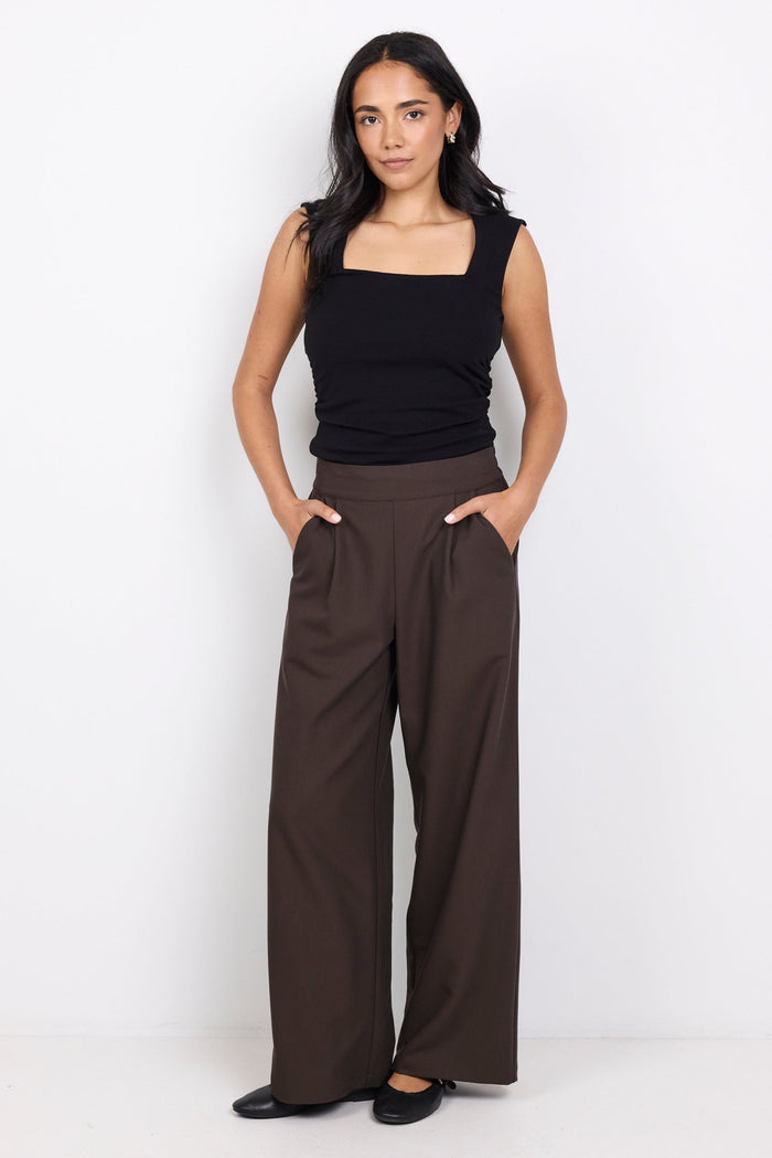 Woman wearing a black top and brown wide-leg pants on a white background