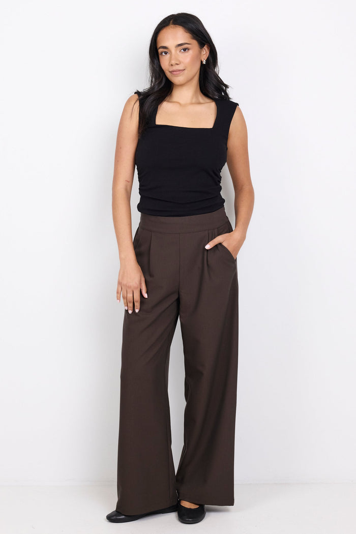 Woman wearing a black sleeveless top and brown wide-leg pants on a white background
