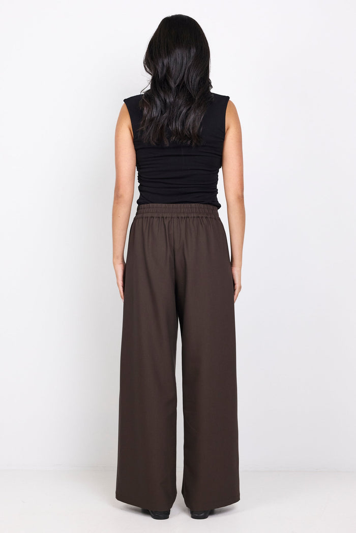 Woman wearing a black sleeveless top and brown wide-leg pants on a white background