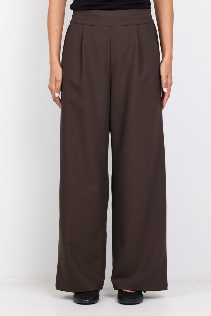 Person wearing brown wide-leg pants and a black top on a white background