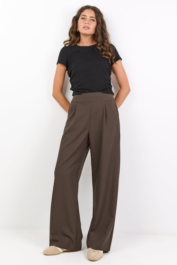 Woman wearing a black top and brown wide-leg pants on a white background