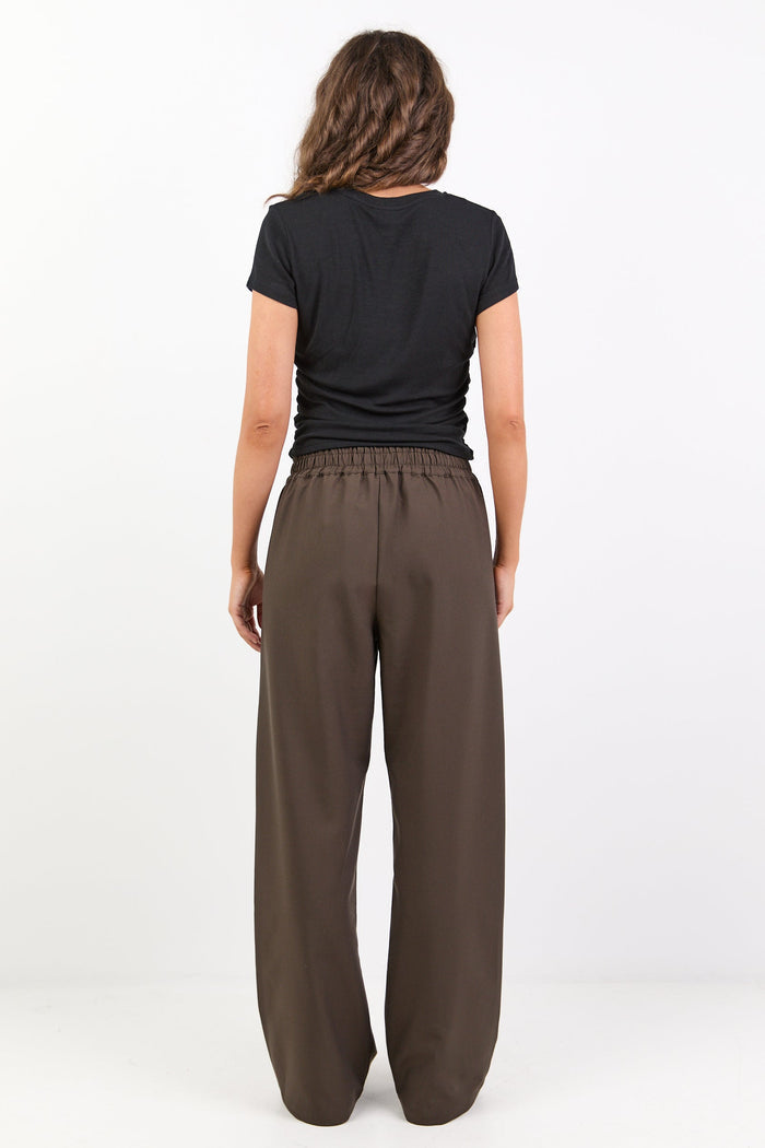 Person wearing a black t-shirt and brown wide-leg pants on a white background