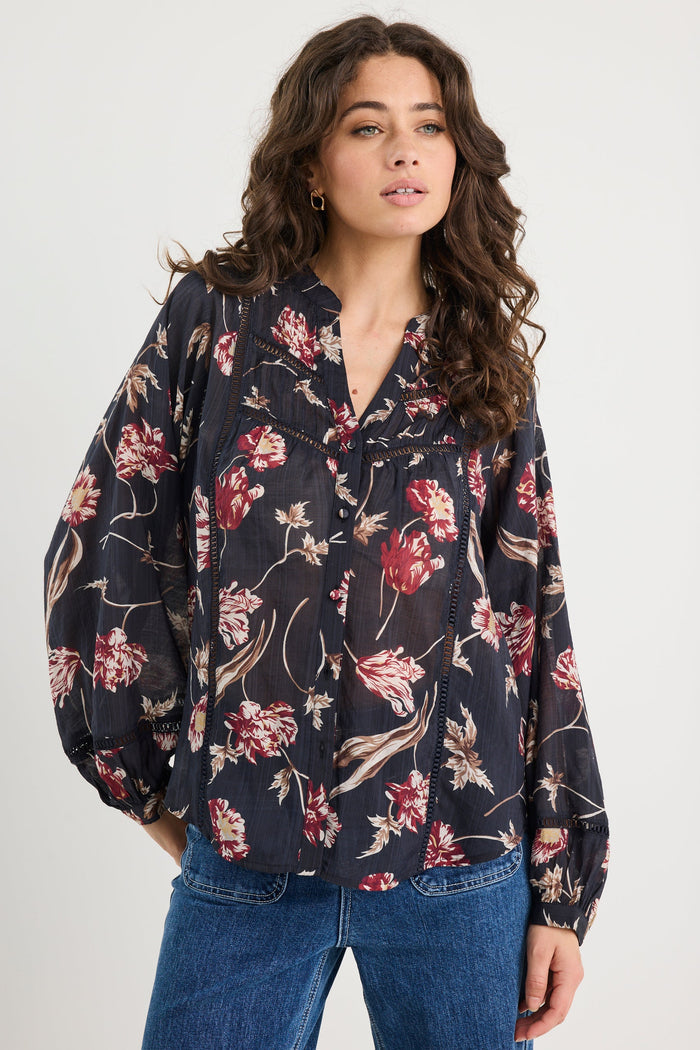 Woman wearing a floral blouse and jeans against a white background