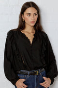 Woman wearing a black blouse and blue jeans against a white brick wall.