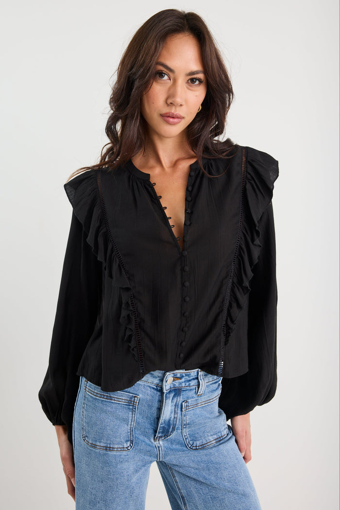 Woman wearing a black blouse with ruffled shoulders and blue jeans on a white background