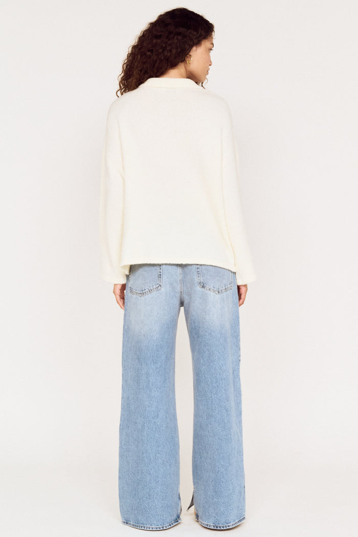Person wearing a white sweater and light blue jeans on a white background