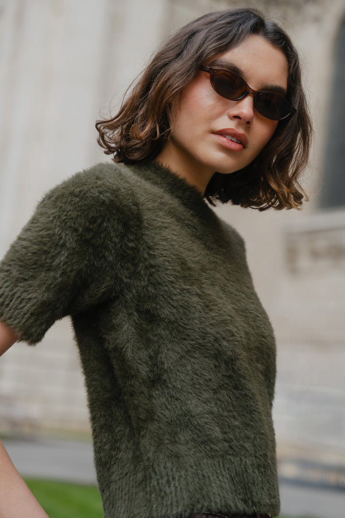 Woman wearing a green sweater and sunglasses with a blurred background
