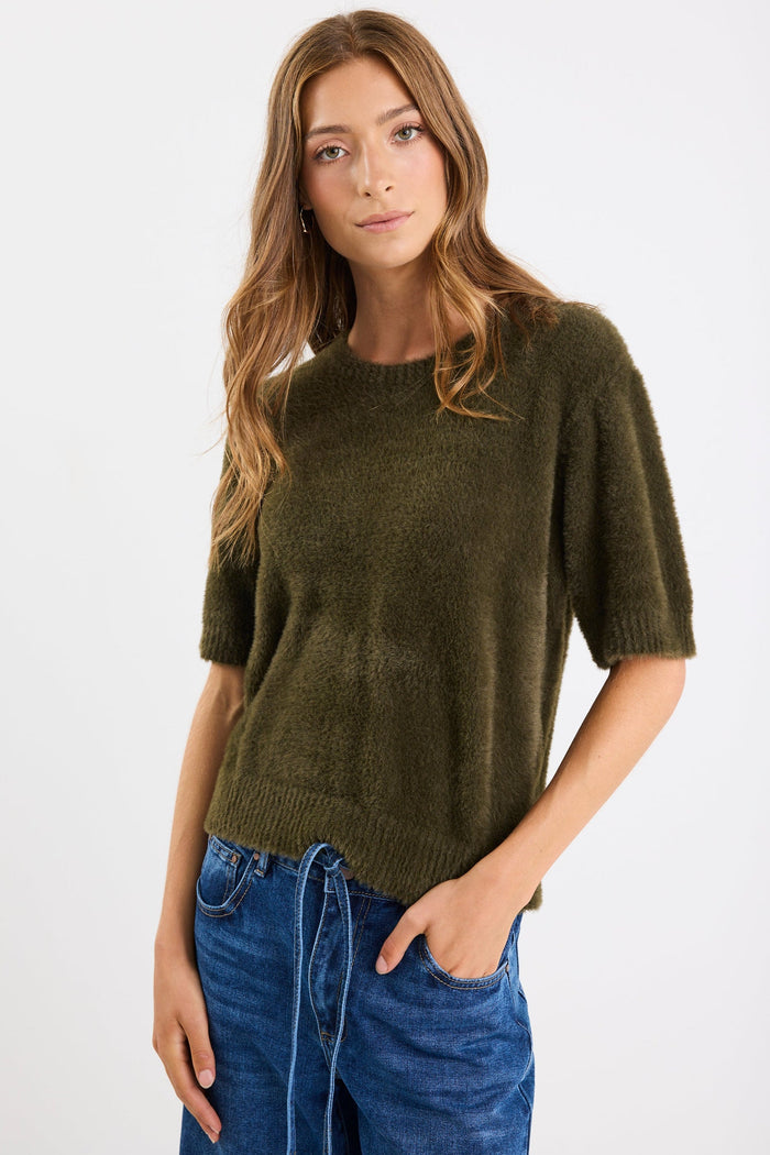Woman wearing an olive green sweater and blue jeans on a white background