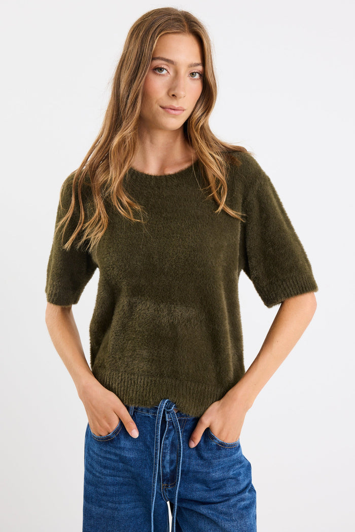 Woman wearing a green sweater and blue jeans against a white background
