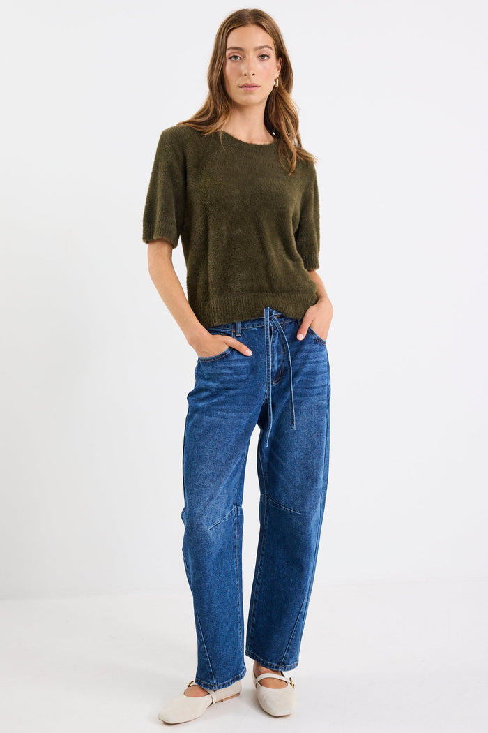 Woman wearing a green sweater and blue jeans on a white background