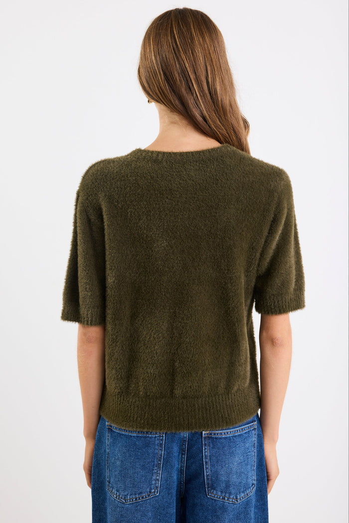 Person wearing a green sweater and blue jeans on a white background