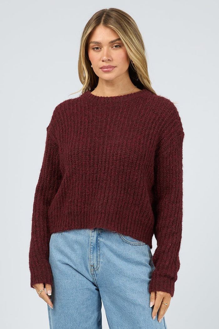 Woman wearing a burgundy sweater and light blue jeans on a white background