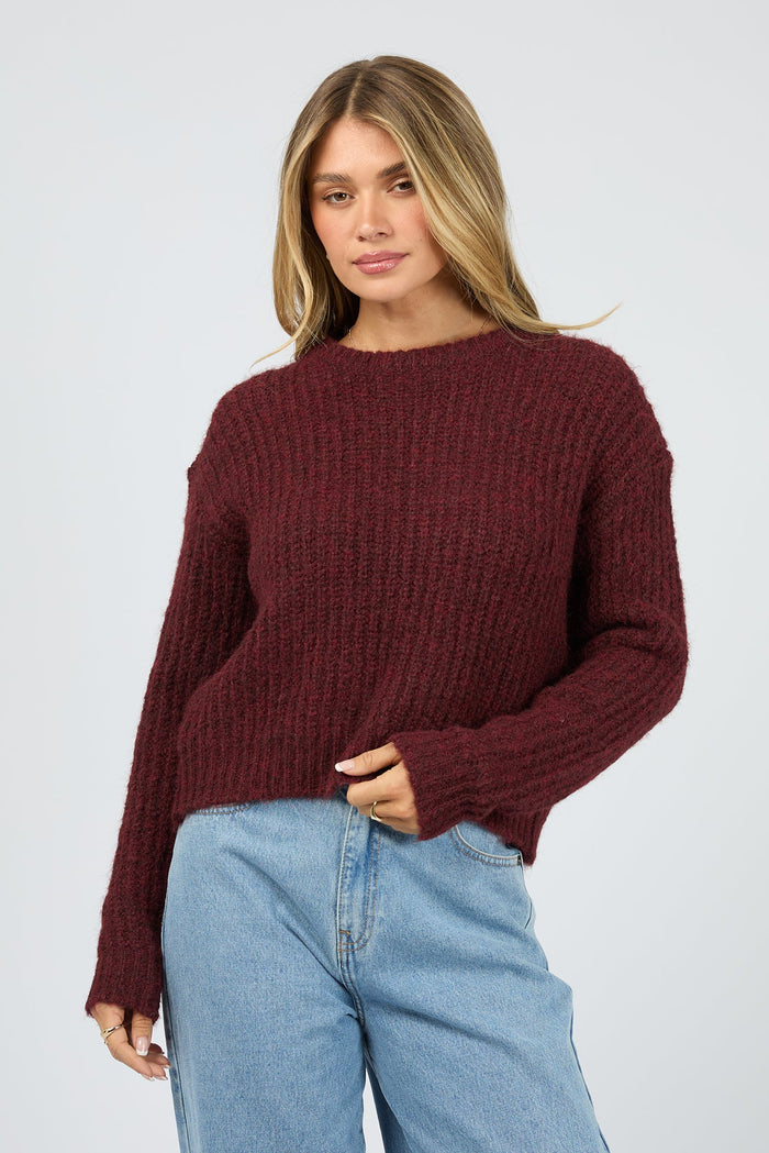 Woman wearing a burgundy sweater and light blue jeans on a white background