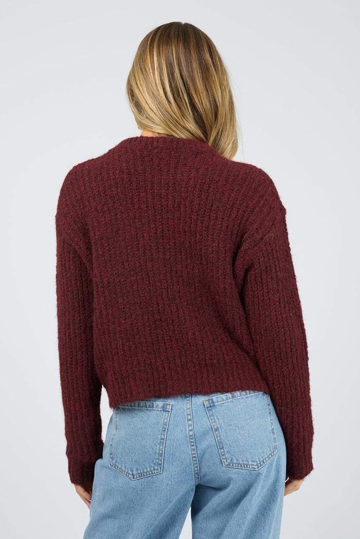 Person wearing a burgundy sweater and blue jeans on a plain background