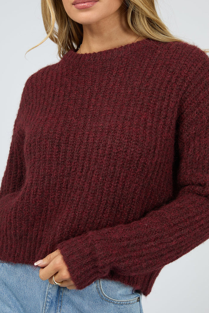 Maroon sweater worn by a person on a plain background