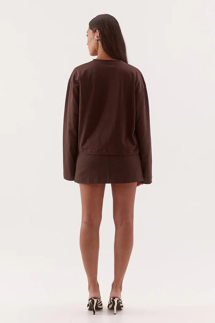 A woman shown from the back wearing a dark brown long-sleeve top and matching mini skirt, paired with black and white patterned heels, against a plain white studio background.