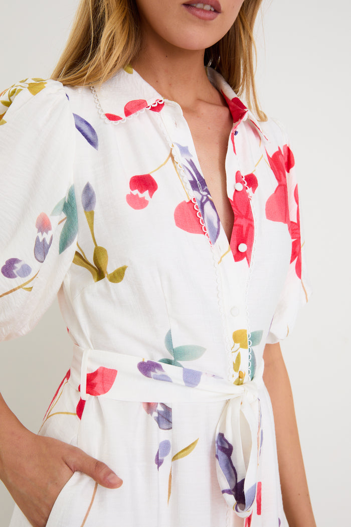 Model wearing a cream midi shirt dress with colourful poppy floral print, puff sleeves and a waist tie.