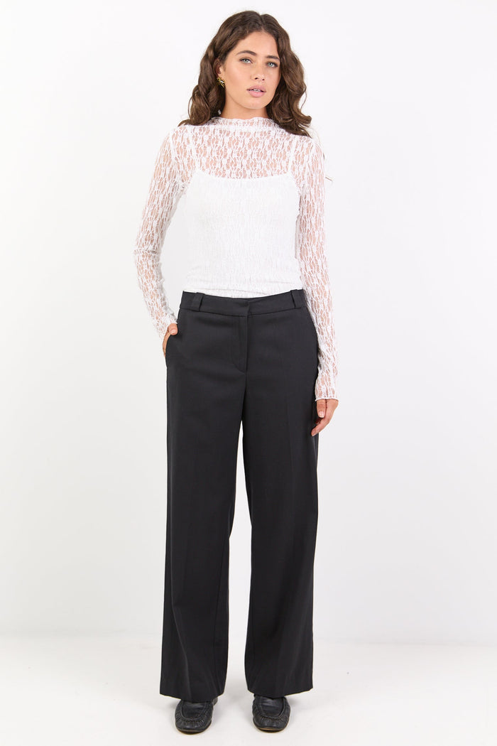 Woman wearing a white lace top and black pants on a white background