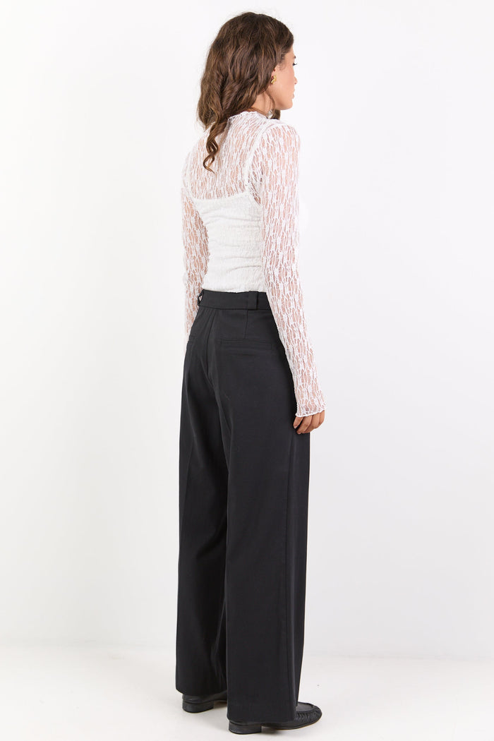 Woman wearing a white lace top and black wide-leg pants on a white background