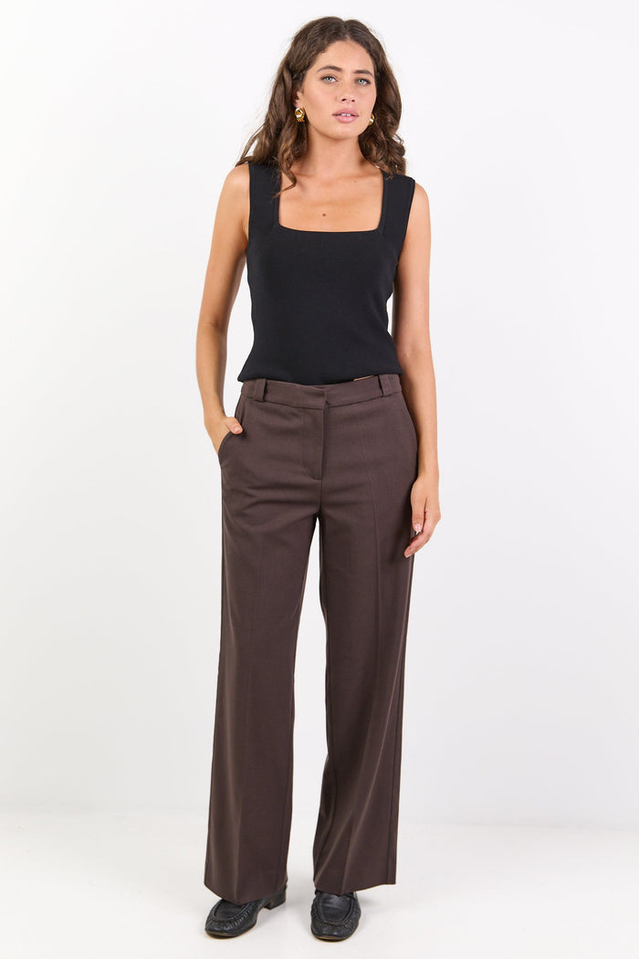 Woman wearing a black sleeveless top and brown pants on a white background