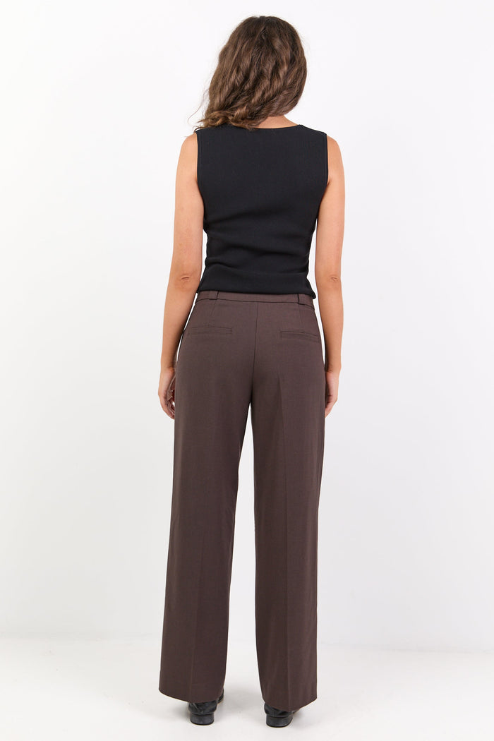Woman wearing a black sleeveless top and brown wide-leg pants on a white background