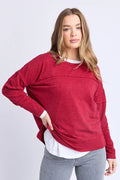 Woman wearing a red sweater over a white shirt with gray pants on a light gray background