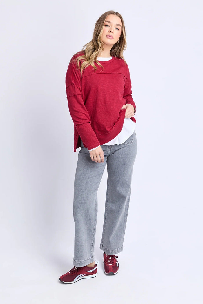 Woman wearing a red sweater, light gray jeans, and red shoes on a white background
